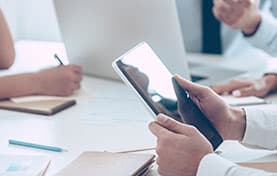 people at a meeting table and one with a tablet