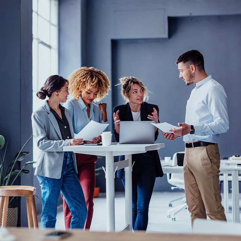 Team of four colleagues using laptop computer and business papers while discussing process during a casual meeting in the office